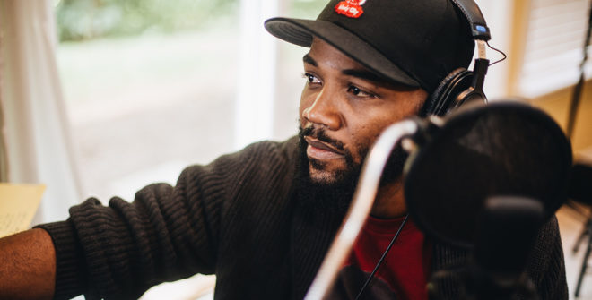 Author/creator A.D. Carson seated in front of a microphone with headphones, looking into the distance.