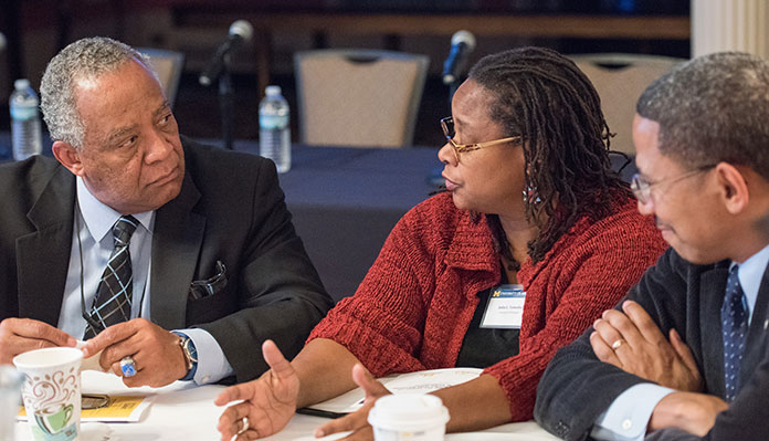 Three people of color siting around a table in discussion at what appears to be a professional conference.